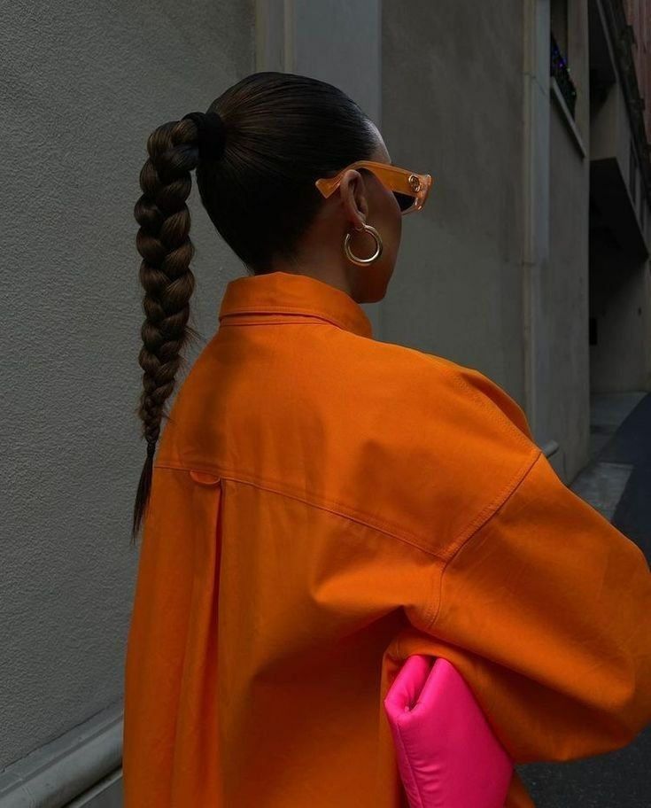 Žena otočená zády mající na sobě oversized oranžovou bundu a držící svítivě oranžovou kabelku v podpaží.